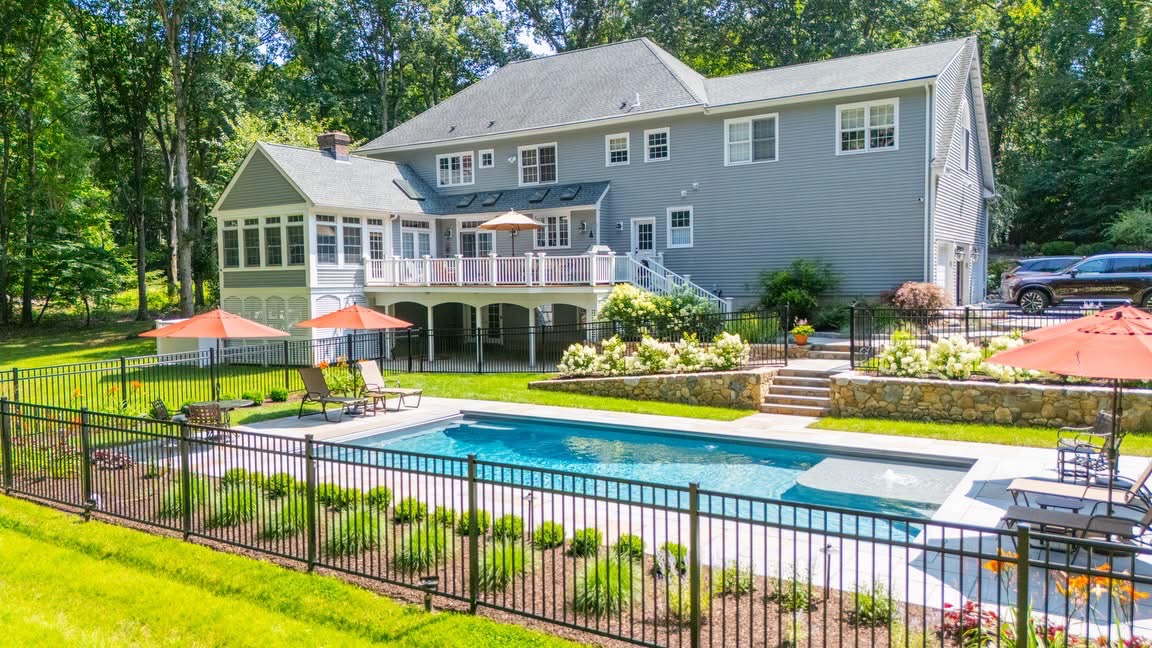 A rear yard with fenced pool, terraced stone walls, layered plantings, and a covered porch