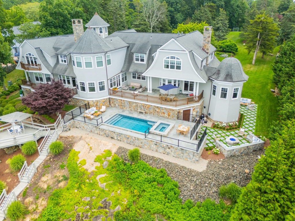 Aerial view of a shingle style home with a raised stone terrace, pool, spa, and fire pit lounge