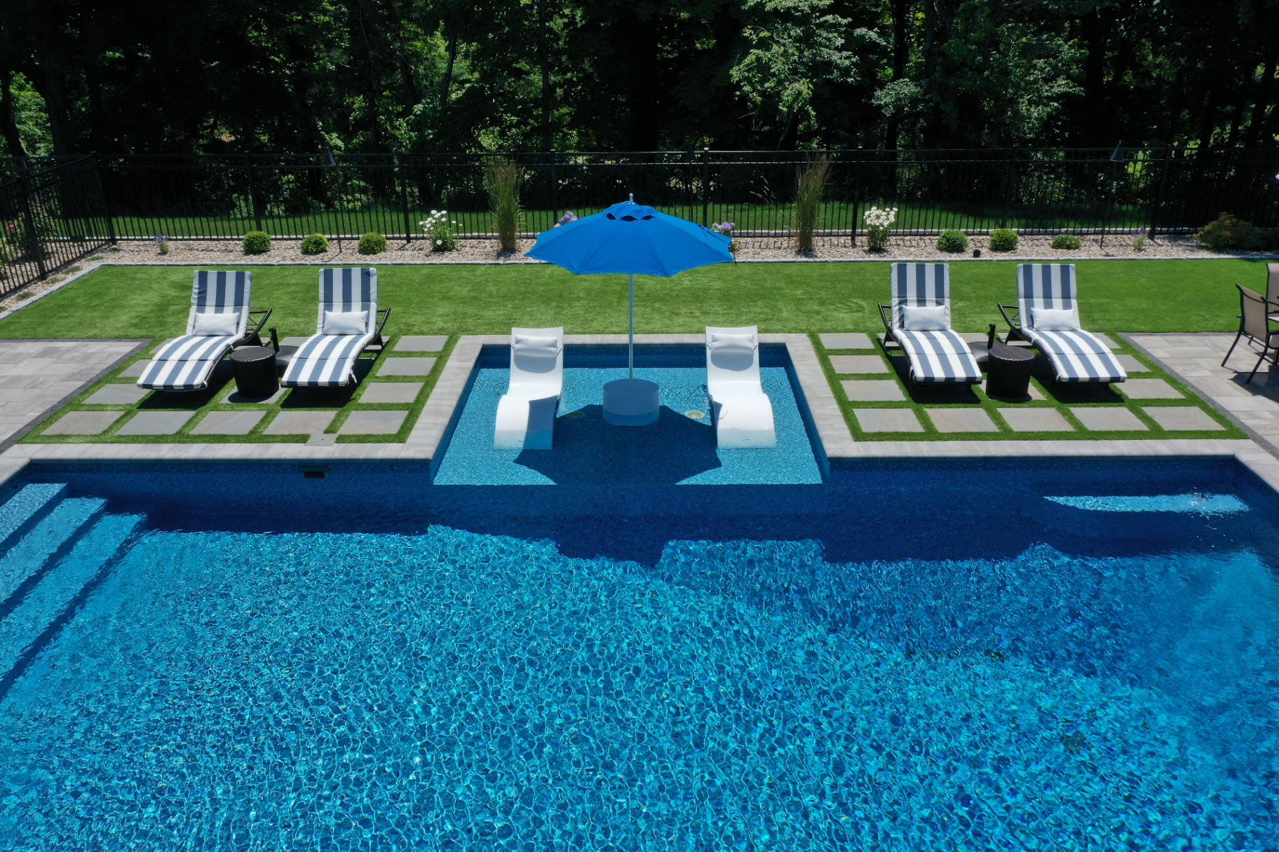 Aerial view of a completed pool, lawn, and geometric patio zones across an outdoor property.