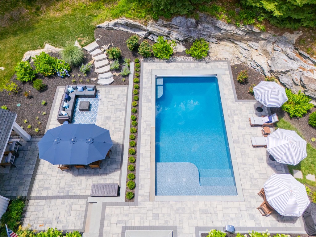 Aerial view of a rectangular pool, paver terrace, dining umbrella, and clipped boxwood border.