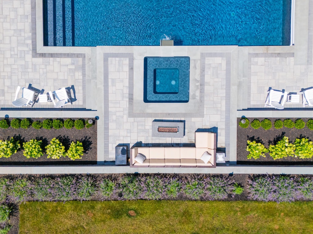 Overhead view of an infinity pool, sunken spa, linear fire table, and symmetrical planting beds