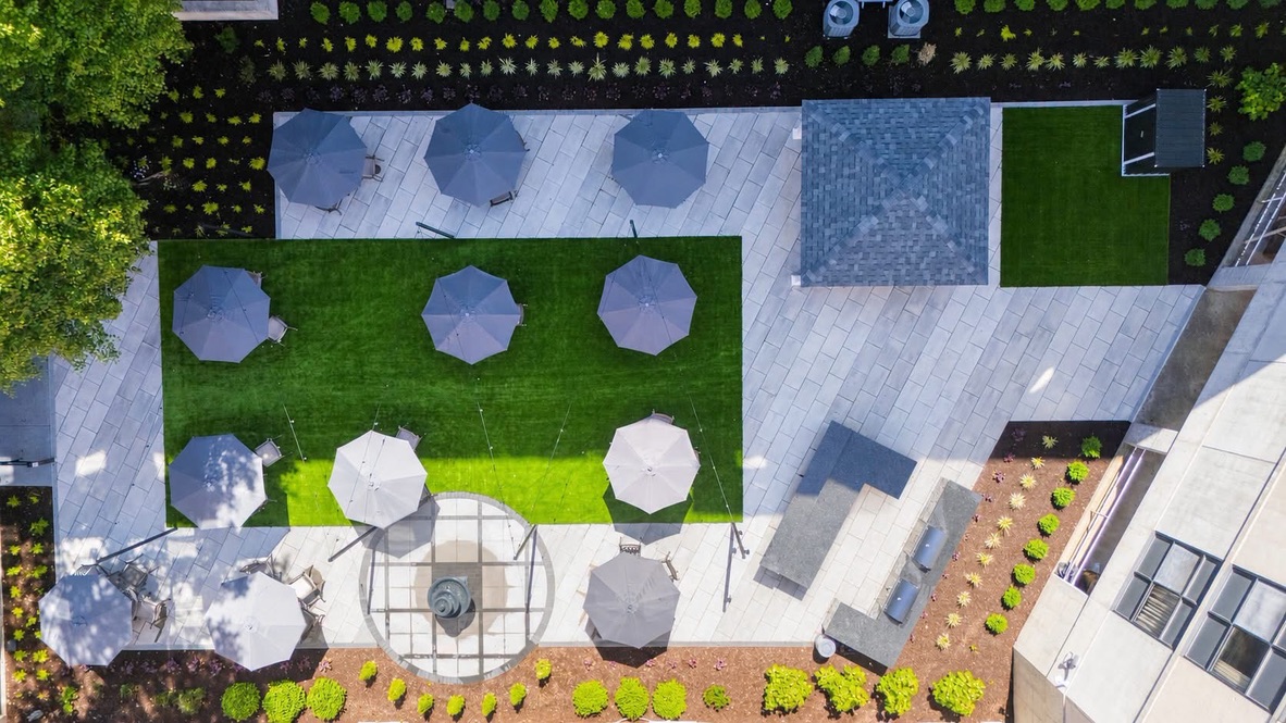 Aerial view of a paver courtyard with a lawn panel, shade umbrellas, and perimeter garden beds