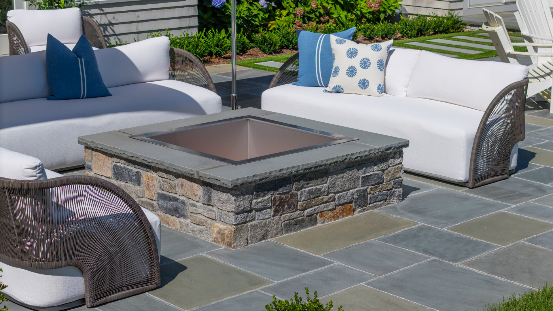 A bluestone patio with stone-clad fire pit and cushioned lounge seating