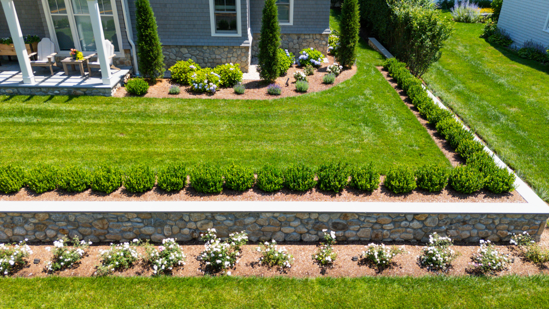 A formal boxwood-lined lawn with stone retaining wall and rose border, showing structured property zones